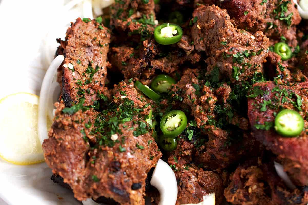 bihari kabab, garnished with green chilies, sliced onions and lemons are plated and ready to eat.