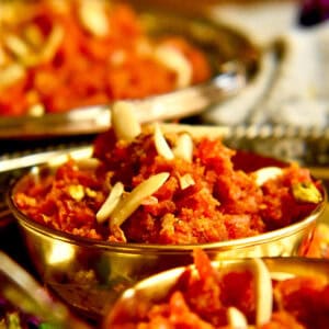 Small gold bowls filled with gajjar ka halwa, garnished with nuts are being served in a tray.