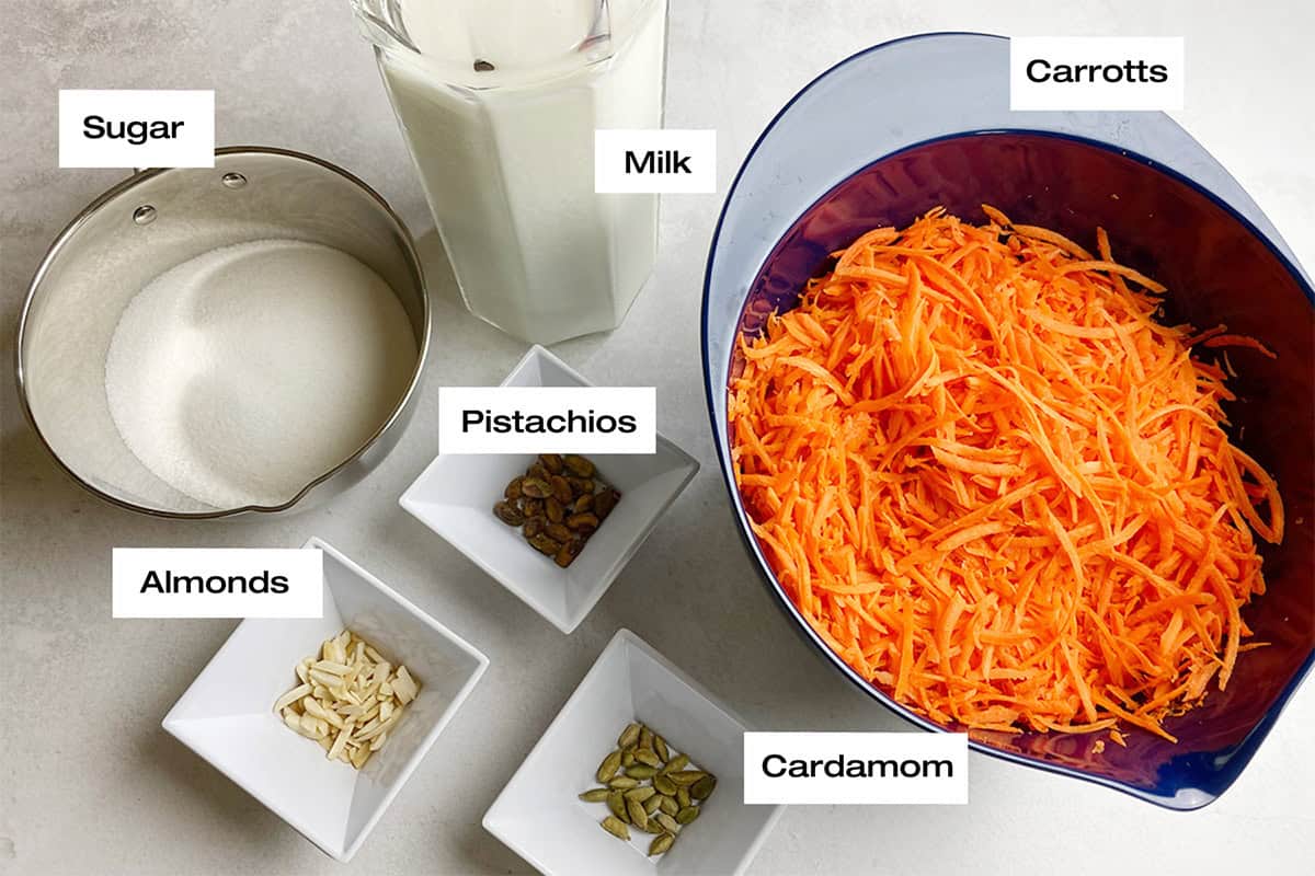 Measured ingredients ready to cook a carrot pudding recipe are spread on a white kitchen counter.