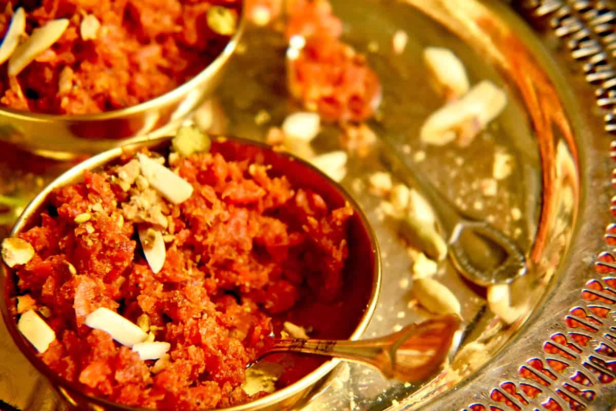 Half eaten Pakistani carrot pudding in a small gold bowl resting on a silver tray and garnished with nuts.