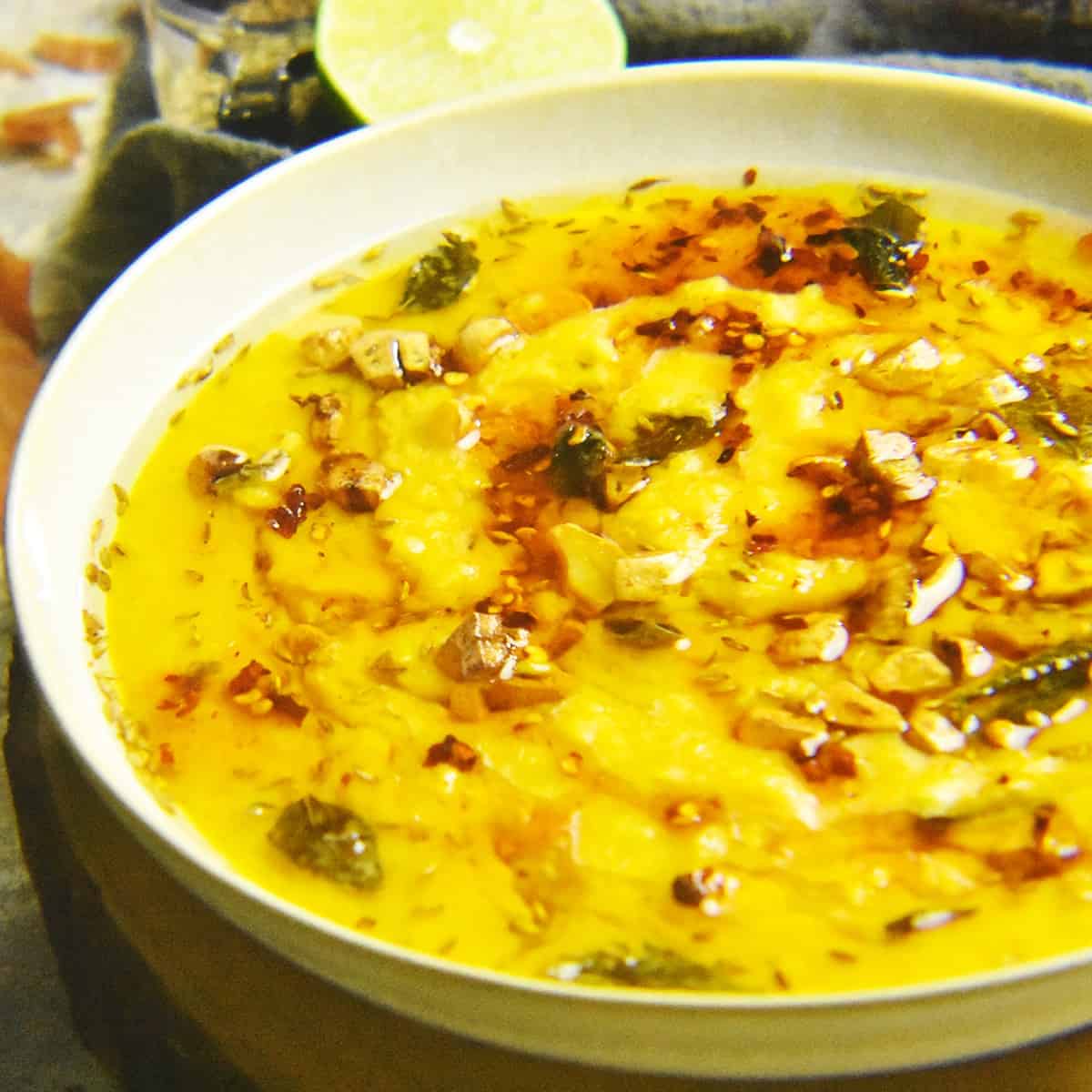 white bowl filled with moong masoor dal topped with a tempering of herbs and spices.