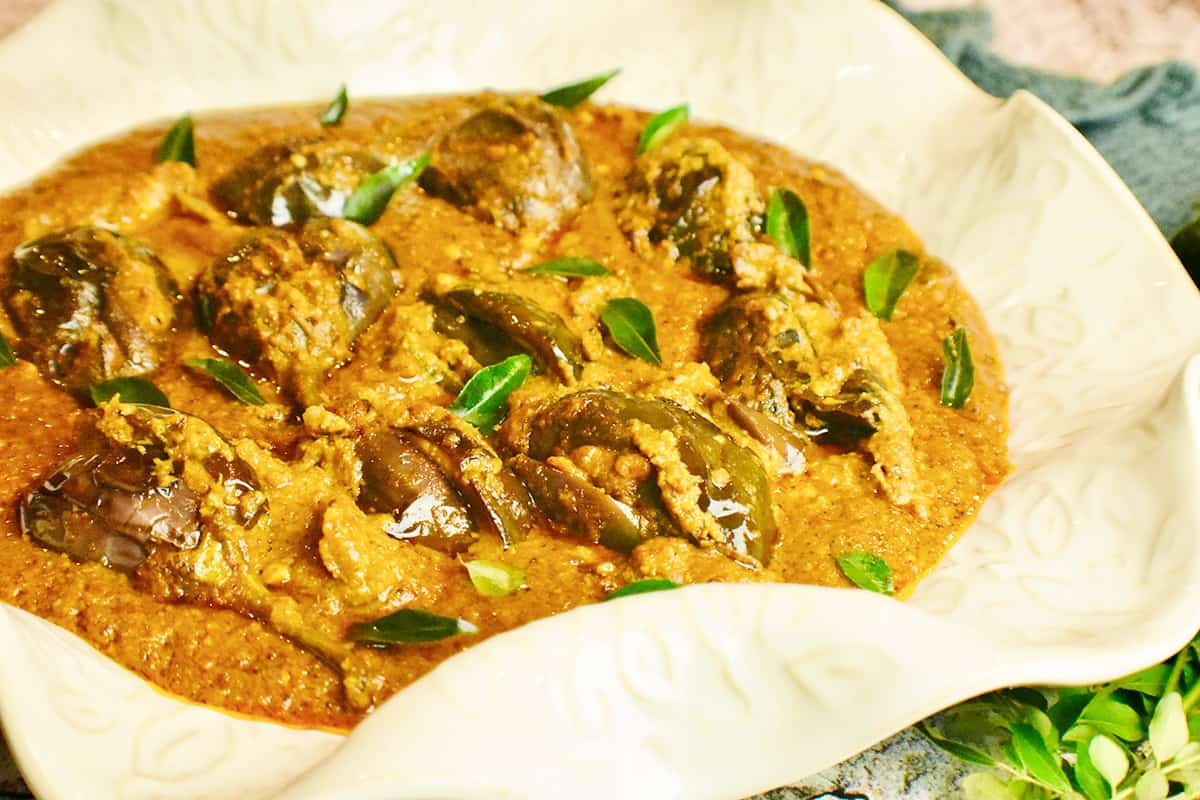 White dish filled with Hyderabadi bagara baingan (eggplant curry) topped with green curry leaves 