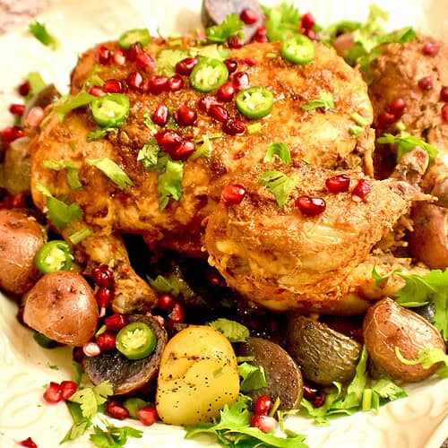 Pakistani steam roast is being served in a white platter with a side of potatoes and a garnish of pomegranate seeds.