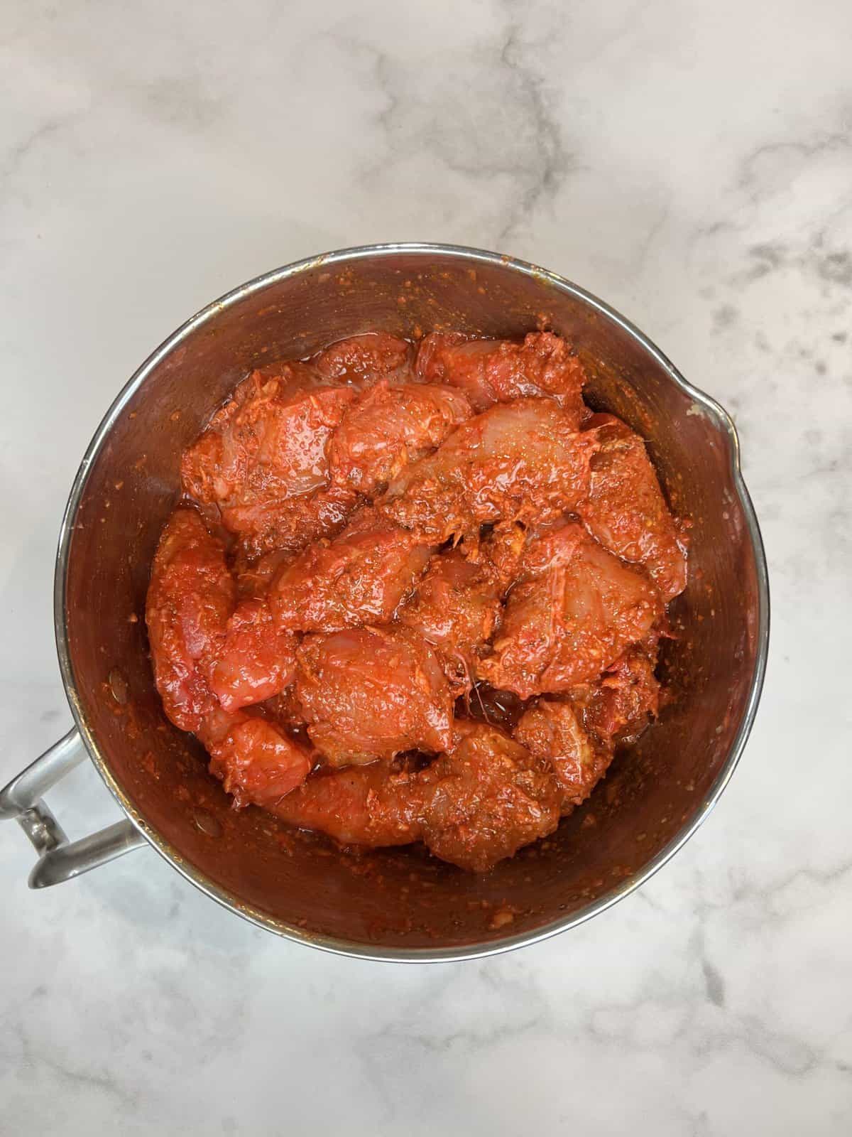 white marble counter with a silver bowl filled with marinated chicken tikka boti.