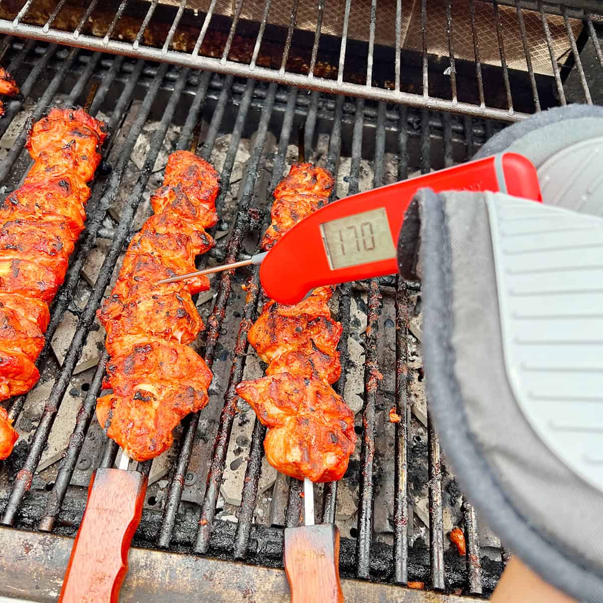 A thermometer being used to check the temperature of meat on a grill.