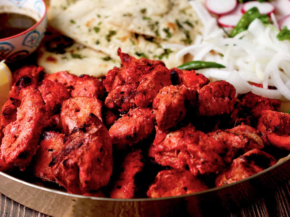 A platter with grilled chicken tikka boti, naan, onions and chutney.