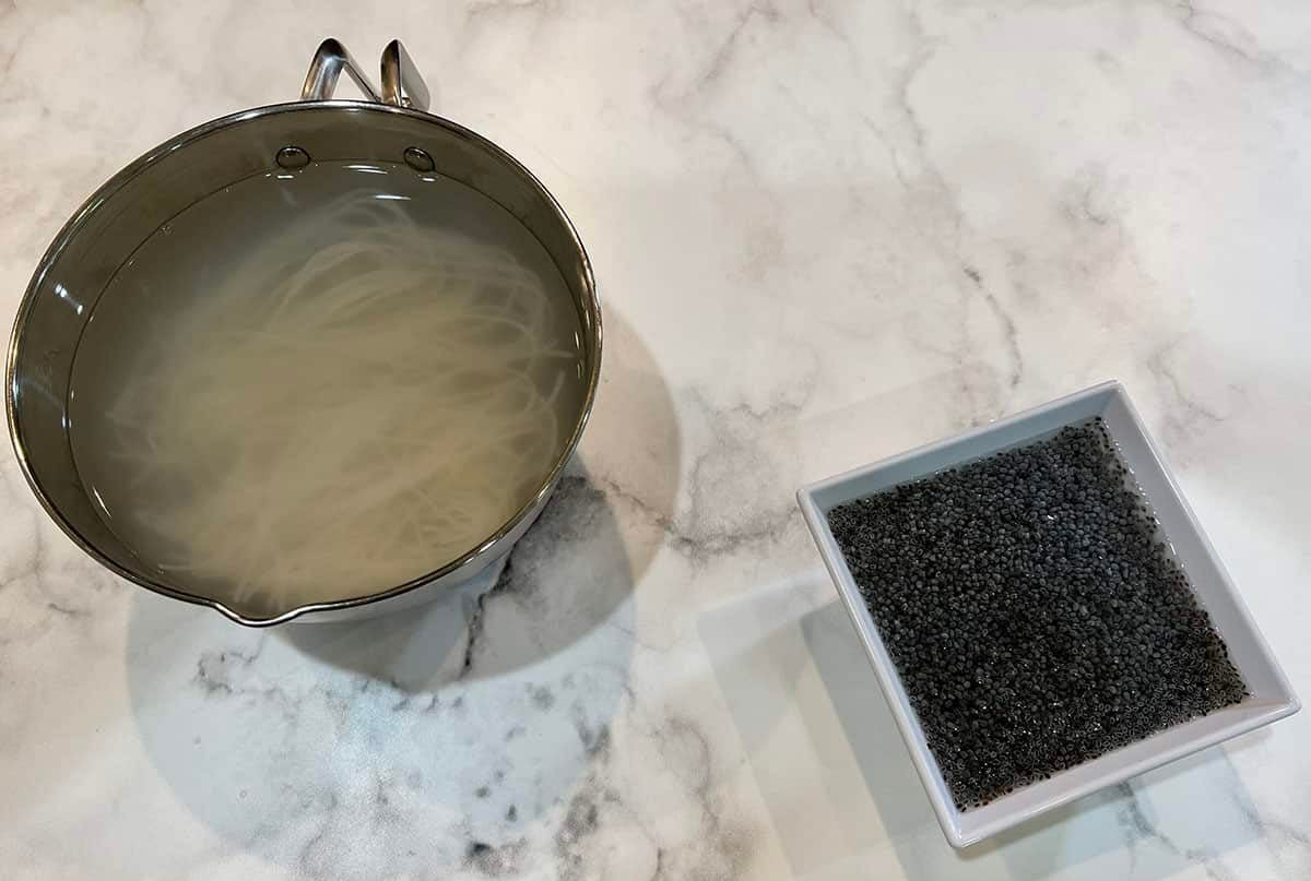 White marble counter top with a stainless steel bowl filled with soaked rice noodles and a white bowl filled with soaked basil seeds.