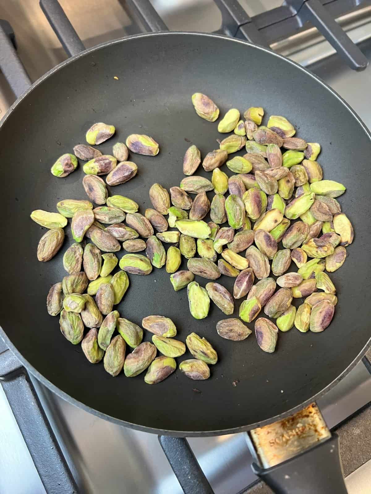 A black frying pan filled with pistachios.