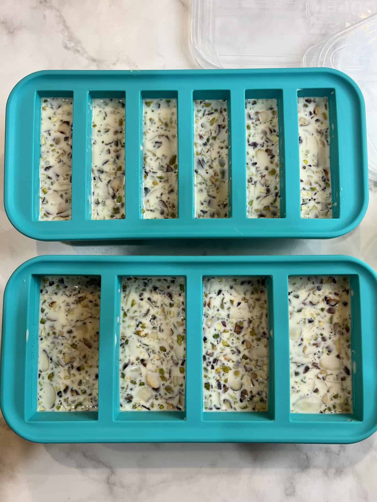 A white countertop with the prepared kulfi mixture in blue moulds ready for the freezer.