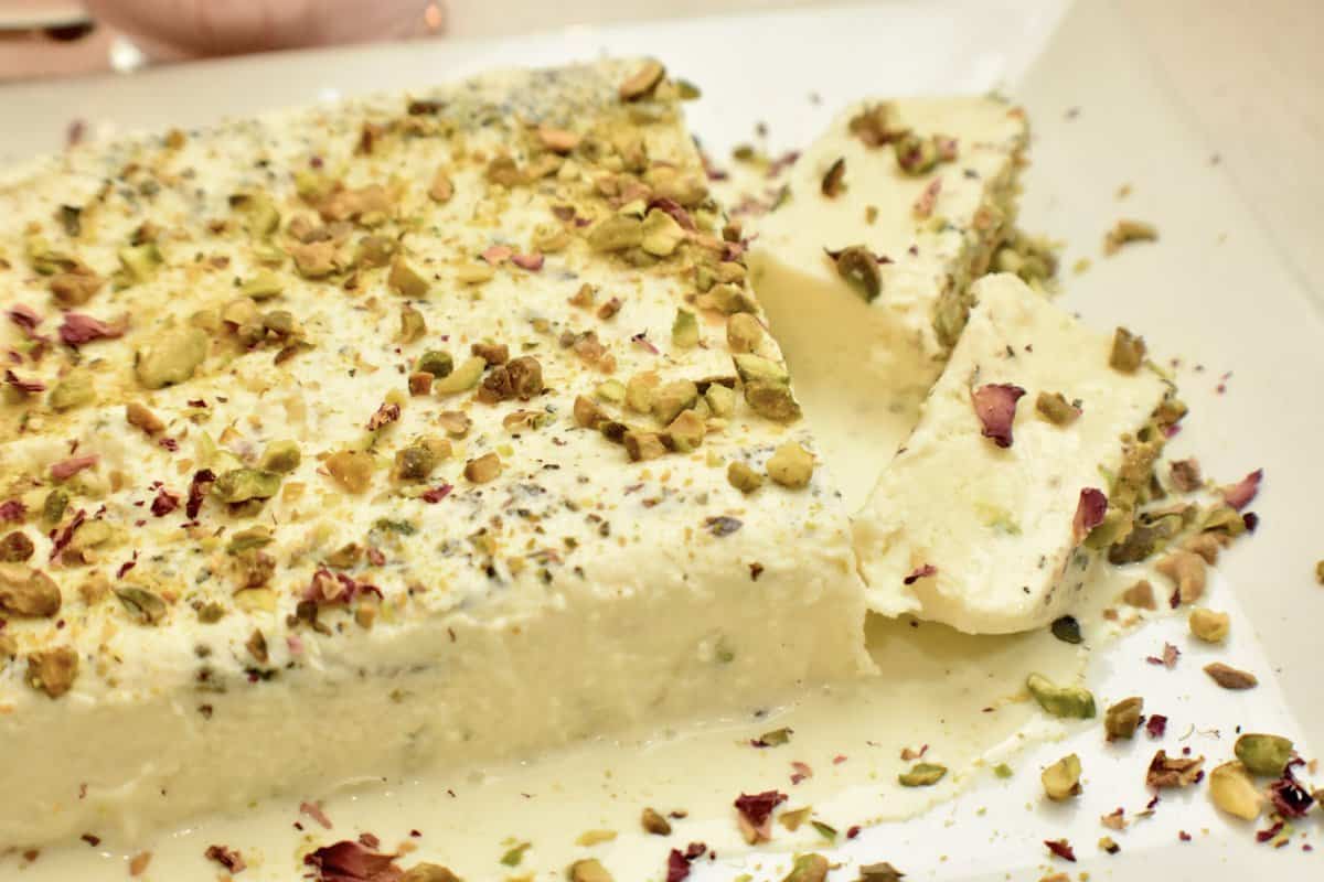 A white platter with kulfi (pakistani ice cream) topped with pistachios and rose petals.