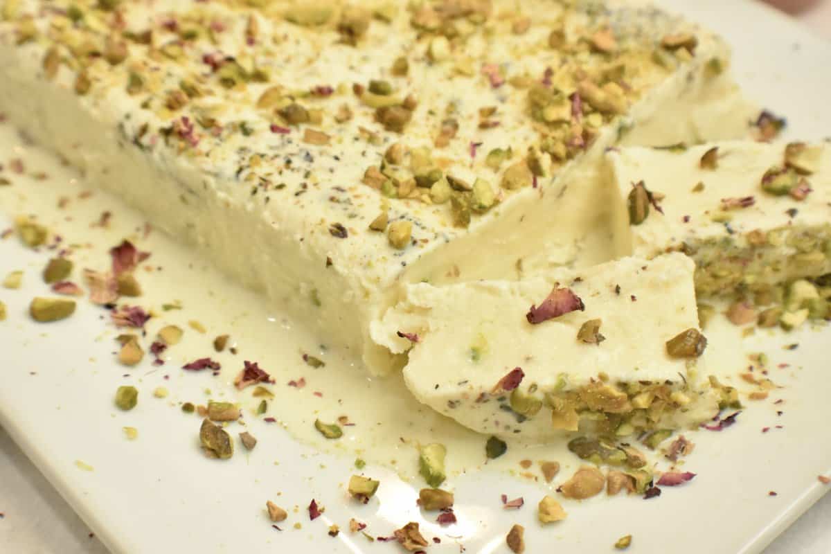 A white platter with kulfi (pakistani ice cream) topped with pistachios and rose petals.