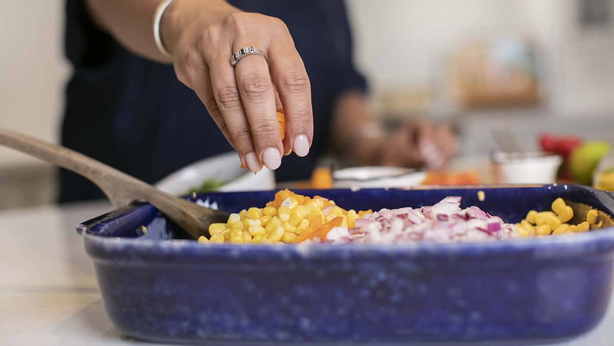 hand adding ingredients to a bright blue dish for corn chaat.