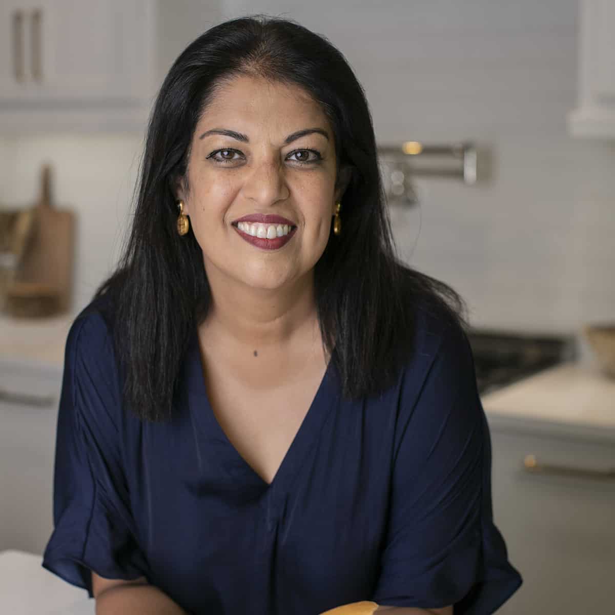 A head shot of Nosheen Babar for her story in a blue shirt leaning on a white kitchen counter.