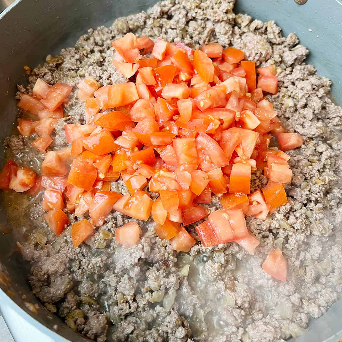 Chopped tomatoes and ground beef being cooked together.
