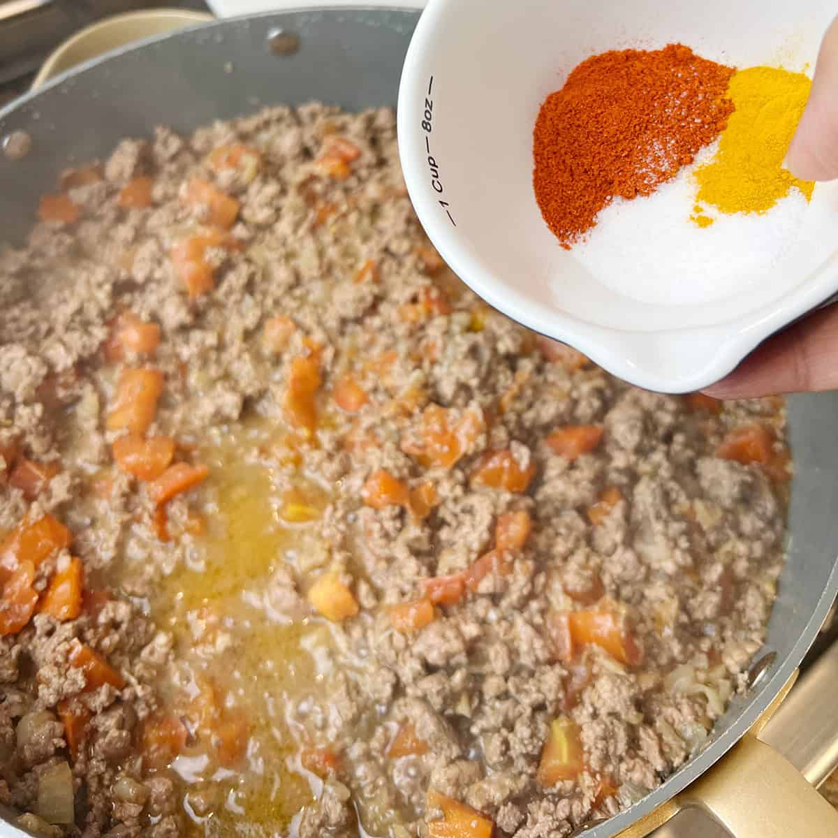 Spices being added to an aloo keema recipe.