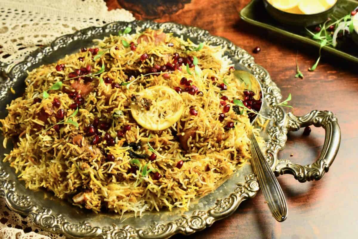 A large silver tray full of biryani is set on a wooden table.