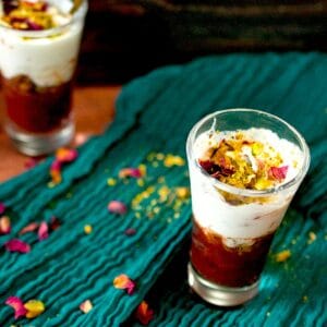 Small shot glasses are filled with a chilled date dessert, topped with heavy whipping cream garnished with chopped pistachios and rose petals.