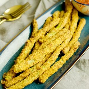An air fryer asparagus recipe is plated in a blue plate that is resting on a greay napkin with gold cutlery.