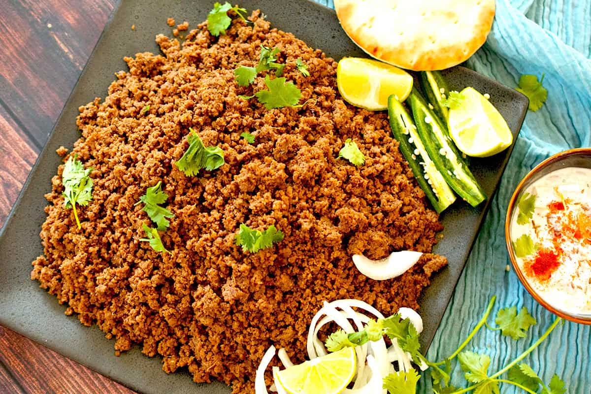 Cooked dum ka keema garnished with sliced onions, chilies and chopped cilantro is served with naan and raita.