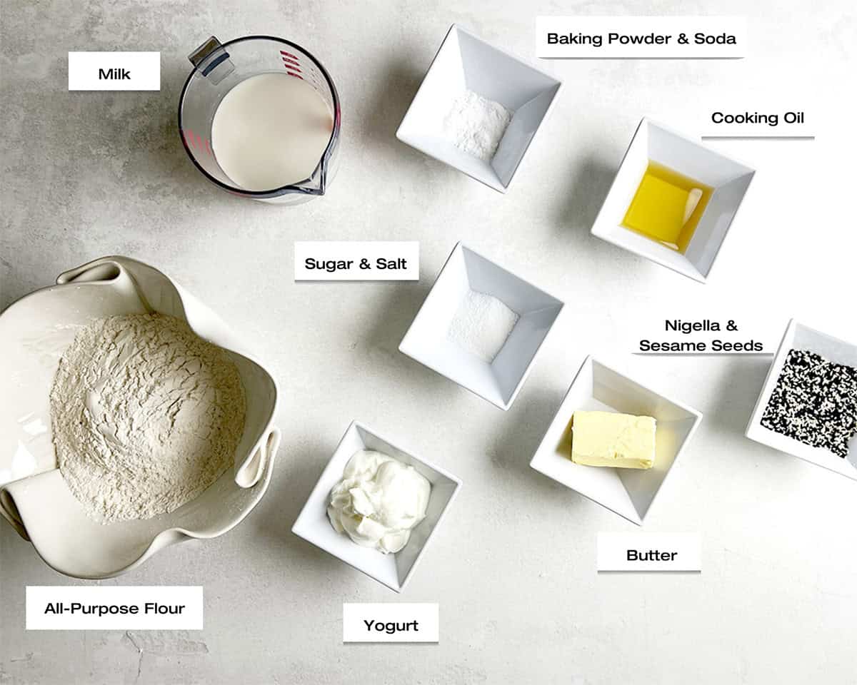 Ingredients for an easy naan recipe are laid out in bowls on a white kitchen counter, ready to cook an easy naan recipe.