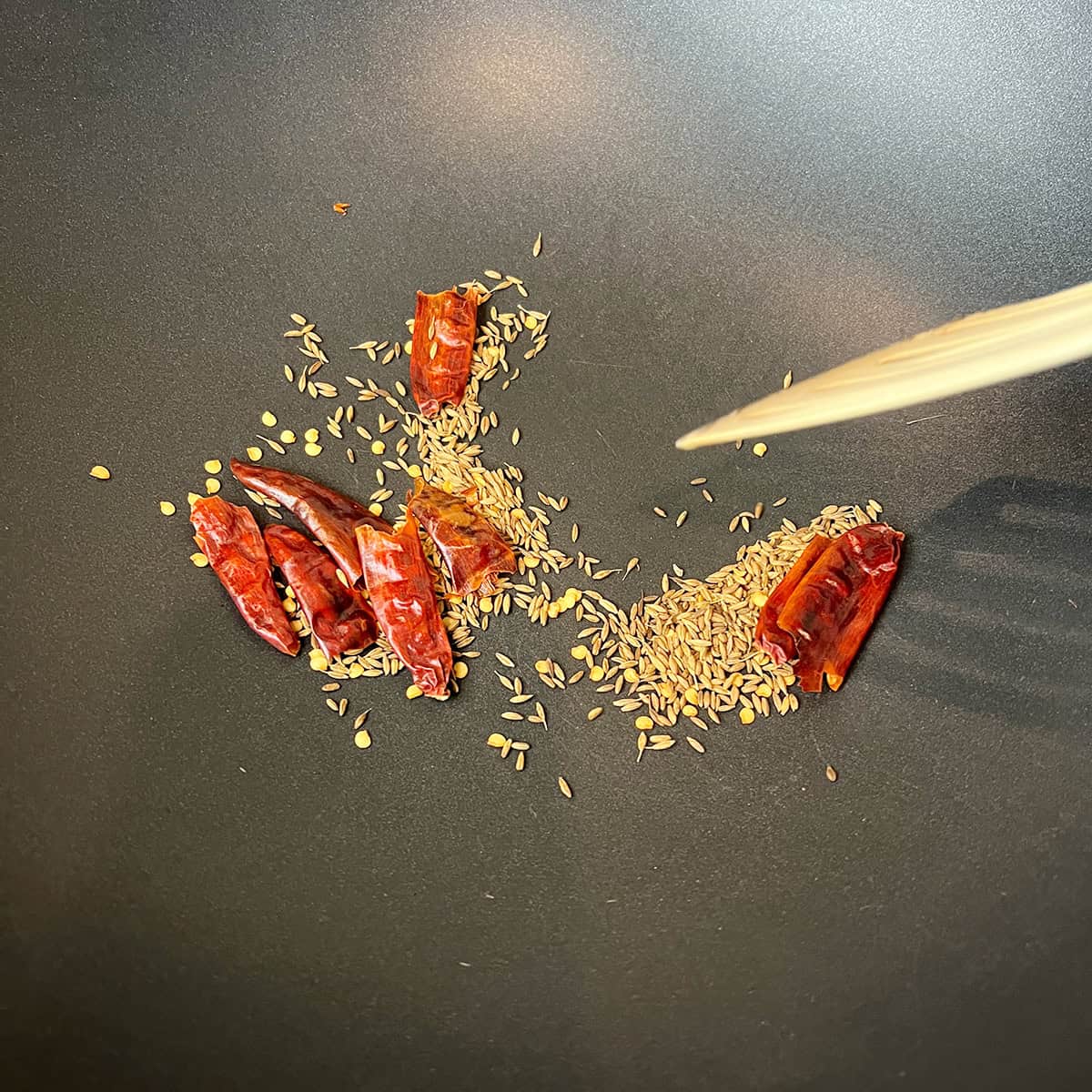 Cumin seeds and dry red chili peppers are being dry roasted in a nonstick pan.