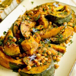 Roasted kabocha squash is topped with crunchy chickpeas and served in a white platter.