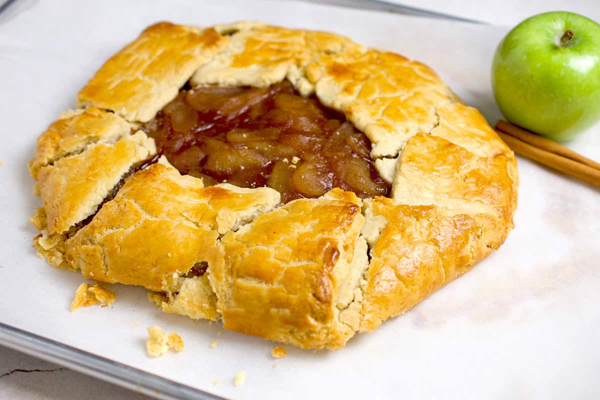 A plated apple galette with a granny smith apple and cinnamon stick in the background.