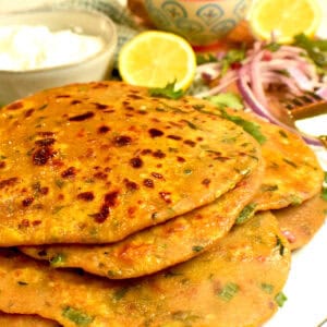 Freshly cooked besan ki roti is plated and served with yogurt, onions and limes.