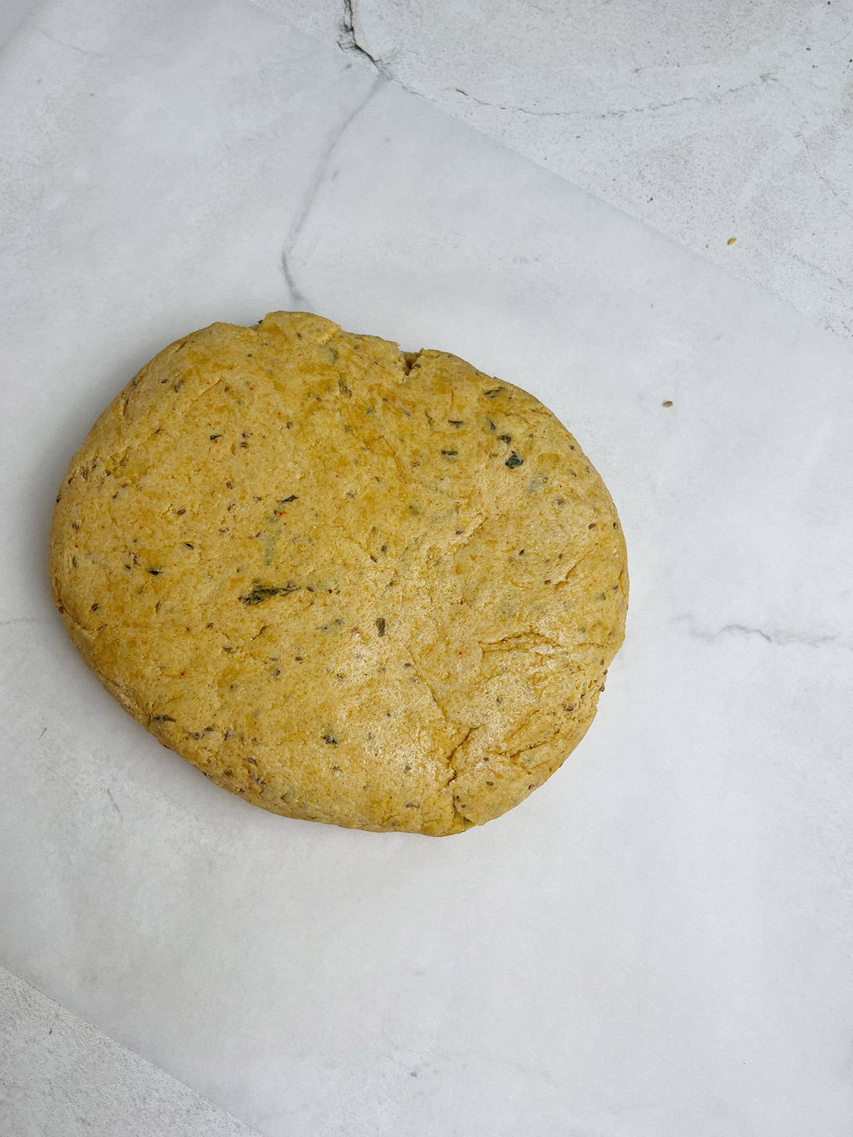 Freshly made cornmeal and whole wheat flour dough is resting on parchment paper, ready to be rolled out.