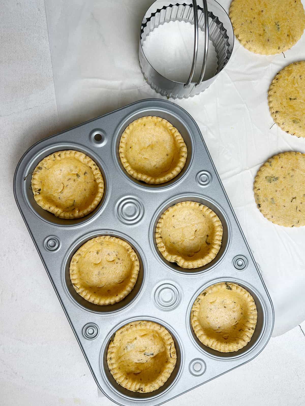 makki ki roti tarts are prepped and ready to be baked in a muffin tin.