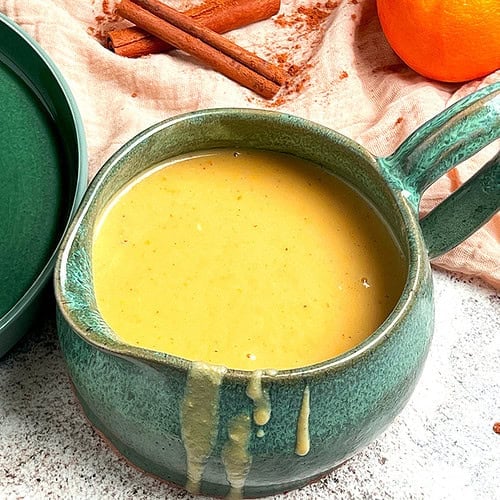 A jug of freshly cooked orange custard sauce is ready to be poured on a cake.