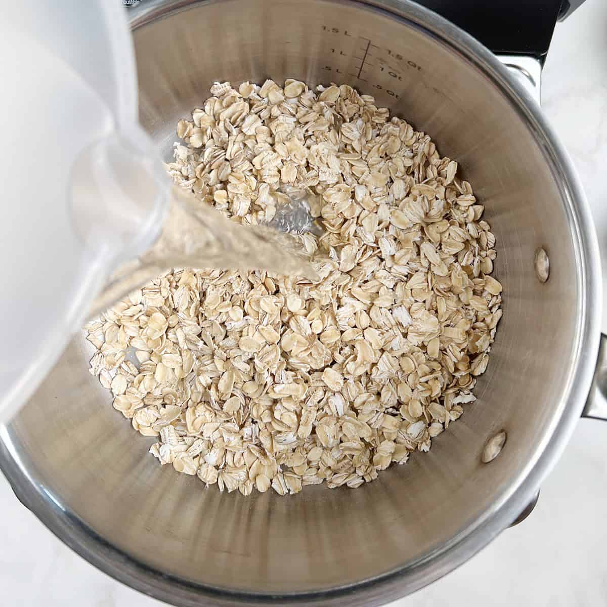 Water being poured over old fashioned oats in a saucepan.