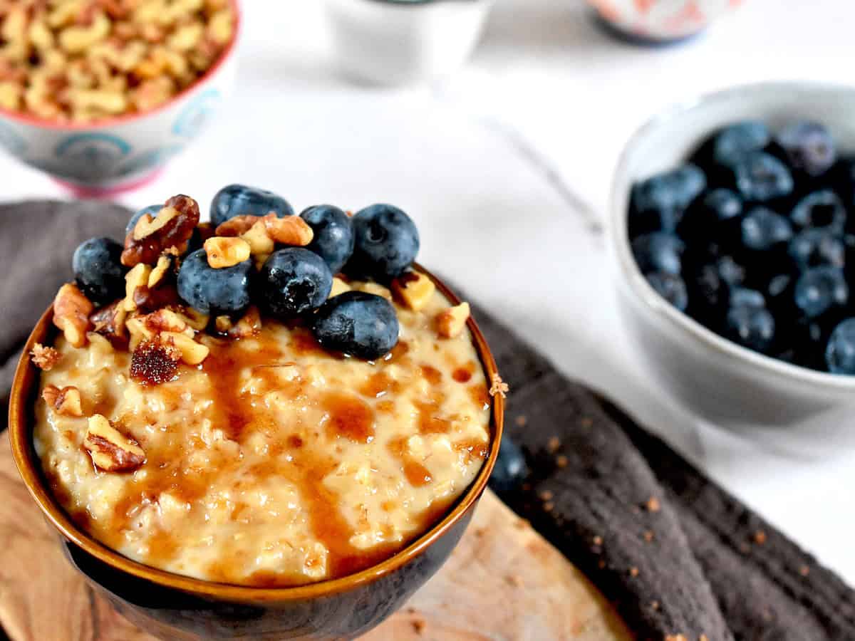 A bowl of warm, creamy oat porridge sweetened with jaggery and topped with blueberries and walnuts.