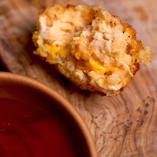 A potato cheese ball with a gooey cheese center and a bowl of ketchup on the side.