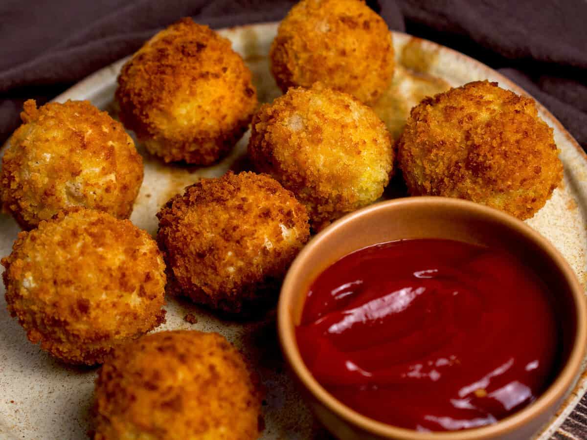 Fried potato cheese balls with a bowl of ketchup on the side.