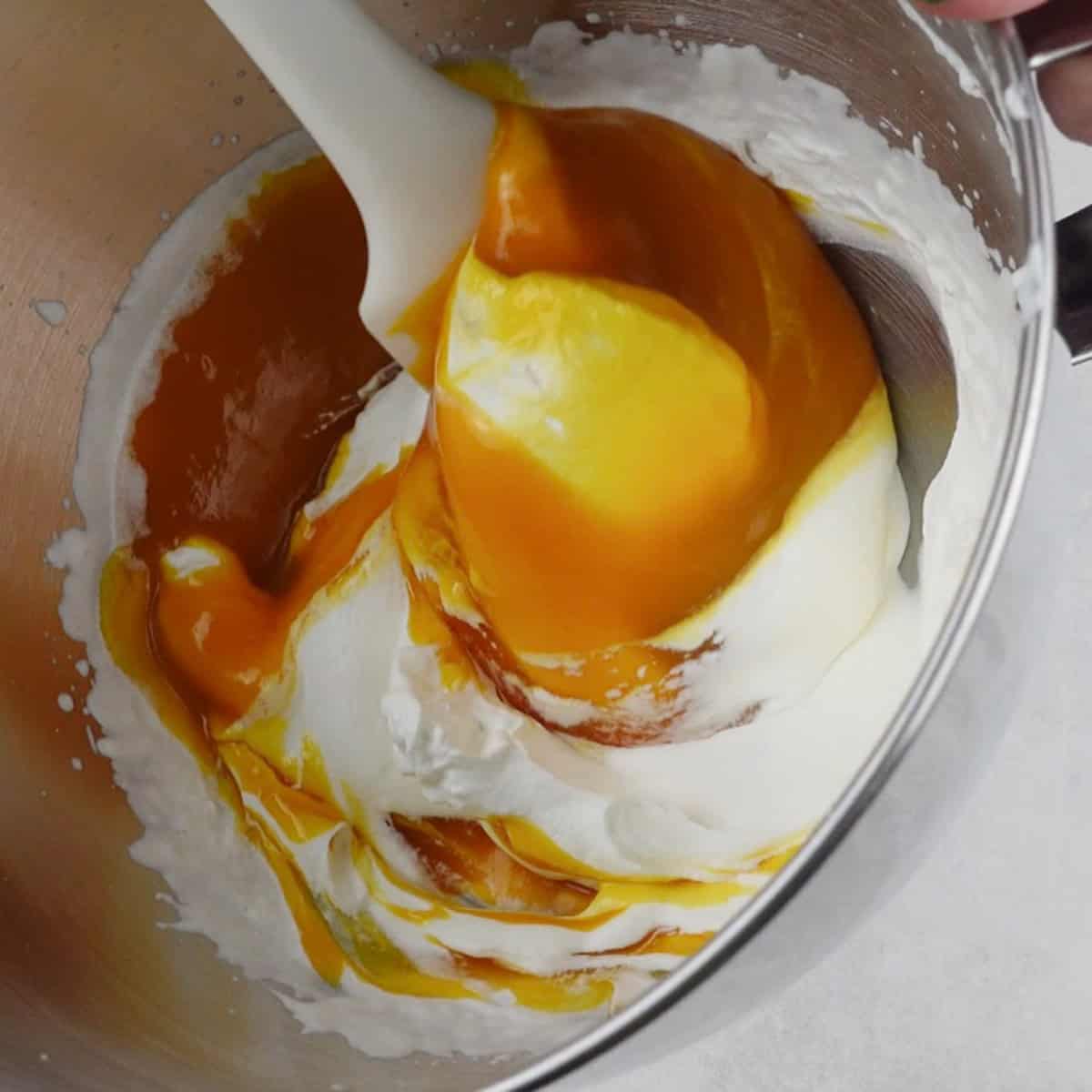Heavy whipping cream and mango puree are being folded for a recipe.